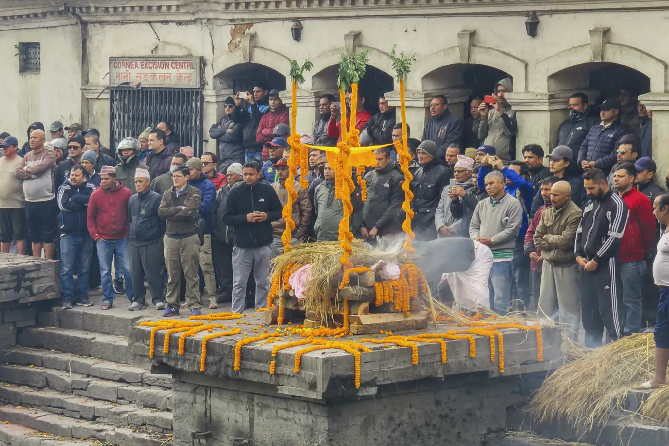 Engalanada la pira y purificado el cadáver los varones asistentes en Katmandú a la cremación presencian la ceremonia.